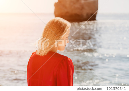 Woman summer travel sea. Happy tourist in long red dress enjoy taking picture outdoors for memories. Woman traveler posing on beach at sea surrounded by volcanic mountains, sharing travel adventure Woman summer travel sea. Happy tourist in long red dress enjoy taking picture outdoors for memories. Woman traveler posing on beach at sea surrounded by volcanic mountains, sharing travel adventure 101570841