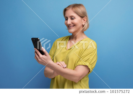 pleasant blond middle-aged woman holding a gadget phone in her hands vertically 101575272