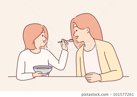 Little girl feeds mother with spoon during breakfast sitting at kitchen table spending time together Little girl feeds mother with spoon during breakfast sitting at kitchen table spending time together 101577261