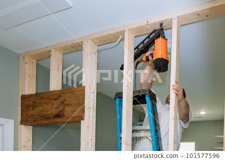 With help of an air hammer, builder nails wooden beams to frames house for construction 101577596