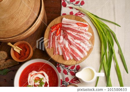 Pieces of salted fatty meat cooked with spices. Salo, bacon, ham. Garlic, fresh onion, spices. A plate of Ukrainian borscht. wooden background Pieces of salted fatty meat cooked with spices. Salo, bacon, ham. Garlic, fresh onion, spices. A plate of Ukrainian borscht. wooden background 101580633