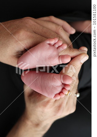 A mother hold the feet of a newborn child in a black blanket on a Black background. The feet of a newborn in the hands of parents. Studio macro photo legs, toes, feet and heels of a newborn. A mother hold the feet of a newborn child in a black blanket on a Black background. The feet of a newborn in the hands of parents. Studio macro photo legs, toes, feet and heels of a newborn. 101581100