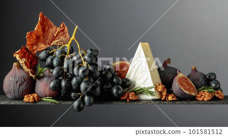 Cheese brie with figs, walnuts, and blue grapes on a dark background. Cheese brie with figs, walnuts, and blue grapes on a dark background. 101581512