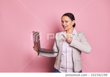 Charming African American business woman, sales manager, confident successful entrepreneur pointing at laptop computer, smiling looking at camera, isolated pink backdrop. Copy ad space. People Career 101582199