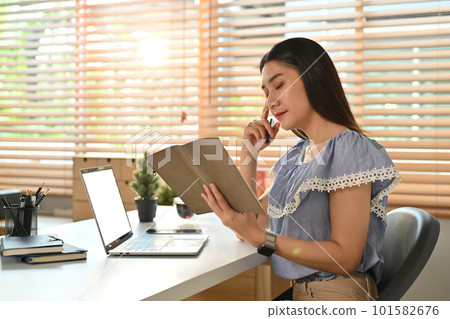 Serious young asian female entrepreneur reading notes in planner or checking her working schedule plan at workplace 101582676