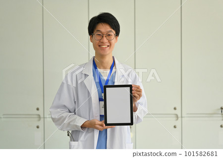 Doctor wearing white uniform showing digital tablet with blank screen for advertisement. Telehealth online applications concept 101582681