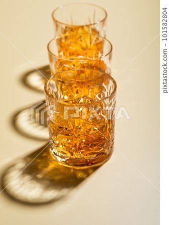 Crystal glasses of single malt whiskey with ice cubes on golden background. 101582804