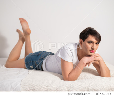 Caucasian transgender man lies on gay bed. Outdoor gay posing in the bedroom. Caucasian transgender man lies on gay bed. Outdoor gay posing in the bedroom. 101582943