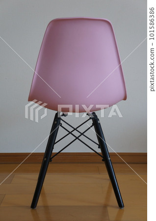 A pink modern chair placed in a room with white walls and light wood flooring 101586386