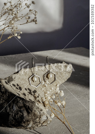 Handmade jewelry earrings made of natural white kasumi pearls and silver on stone and modern concrete background with gypsophila flowers 101589382