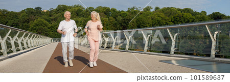 Smiling senior man and lady with mobile phone run along footbridge 101589687