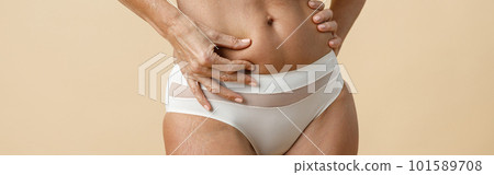 Body of fit mature woman in underwear touching her skin, holding hand on waist, standing isolated over beige background 101589708
