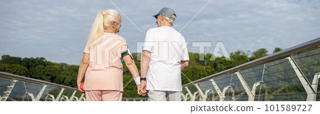 Positive senior woman and man walk holding hands along footbridge after training 101589727