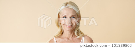 Portrait of beautiful mature woman with blonde hair in white underwear smiling at camera, standing isolated over beige background Portrait of beautiful mature woman with blonde hair in white underwear smiling at camera, standing isolated over beige background 101589803