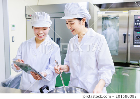 一位身穿白大褂的女廚師一邊準備食物，一邊在廚房的平板電腦上檢查食譜。 101590092