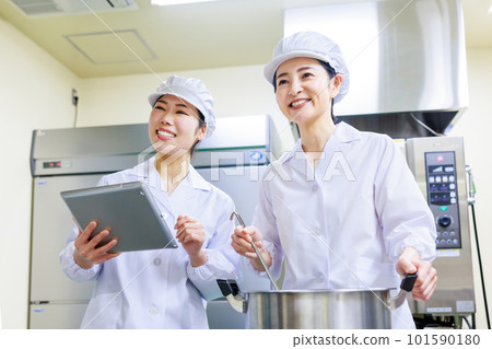 A female cook wearing a white coat cooking in the kitchen 101590180