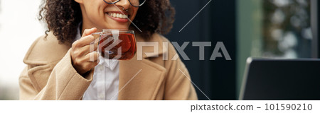 Woman freelancer working remotely and drinking tea while sitting on cafe terrace 101590210