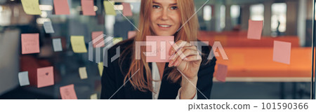 Smiling Businesswoman showing sticky notes with motivational phrases while standing in office Smiling Businesswoman showing sticky notes with motivational phrases while standing in office 101590366