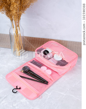 A beautiful pink cosmetic bag with the necessary products for the care of women's skin. Cosmetics, shampoo, creams, makeup brushes in a cosmetic bag against the backdrop of a beautiful women's room. 101590388