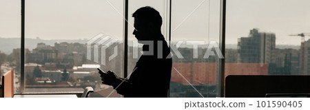 Silhouette of a businessman with phone in his hands standing in office 101590405