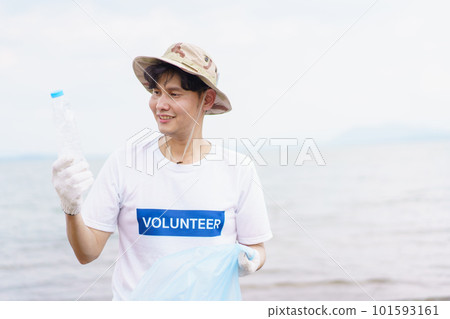 Asian young man picking up a plastic bottle garbage on the beach, male volunteer walking around the beach and collecting - cleaning a plastic waste. 101593161