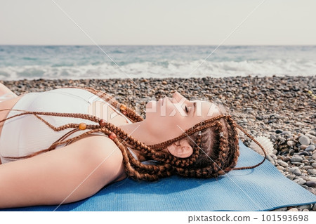 Woman sea yoga. Well looking middle aged woman with braids dreadlocks in white leggings and tops doing stretching pilates on yoga mat near sea. Female fitness yoga routine concept. Healthy lifestyle. 101593698