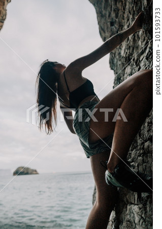 Sports Woman Climbing The Rock. Young woman With slim fit body climbing in volcanic basalt cave with beautiful sea view. The athlete girl trains in nature. Woman overcomes difficult climbing route. Sports Woman Climbing The Rock. Young woman With slim fit body climbing in volcanic basalt cave with beautiful sea view. The athlete girl trains in nature. Woman overcomes difficult climbing route. 101593733