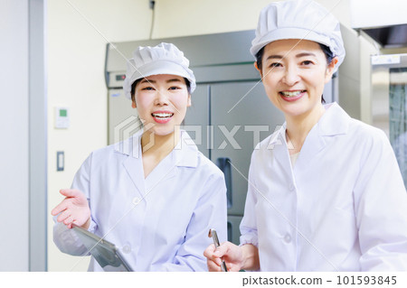 A female cook wearing a white coat prepares food while checking the recipe on a tablet in the kitchen. A female cook wearing a white coat prepares food while checking the recipe on a tablet in the kitchen. 101593845