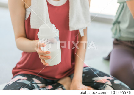 Women drinking protein and water while taking a break in a yoga class at a sports gym 101595576