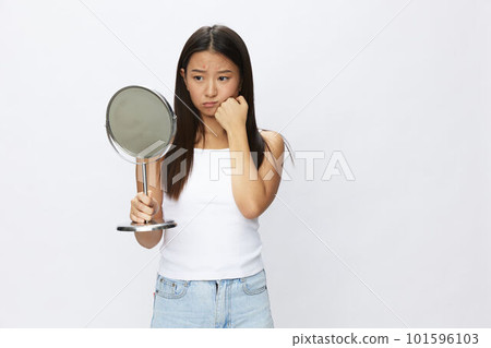 Asian woman with mirror in hand facial skin problems, acne and inflammation, red rash and allergies, chicken pox, sadness from rashes. Facial skin care concept for diseases and nerves 101596103