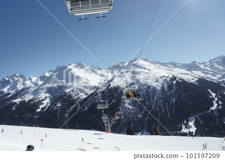 Tourists traveling in ski lifts over snow covered land with mountains in background during winter vacation, winter holiday travel concept 101597209
