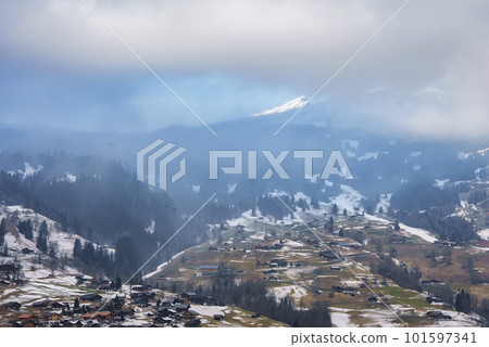 Aerial view of houses and trees on landscape in Grindelwald village with majestic mountains and cloudy sky in background at Jungfrau, Switzerland, winter holiday concept 101597341