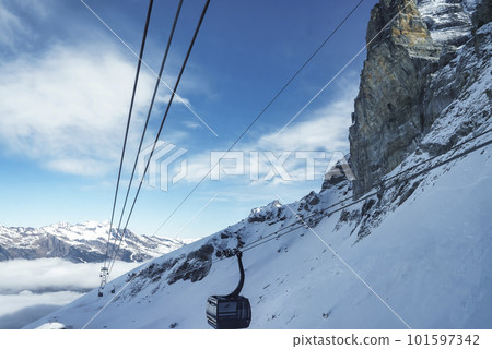 Gondola lift moving on cable over beautiful snowcapped Bernese mountain under cloudy sky at ski resort in Jungfrau, Switzerland, winter holiday and nature concept Gondola lift moving on cable over beautiful snowcapped Bernese mountain under cloudy sky at ski resort in Jungfrau, Switzerland, winter holiday and nature concept 101597342