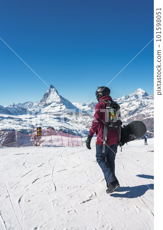 Young snowboarder spending winter holidays in Zermatt, near the famous Matterhorn peak. Male posing in Swiss Alps for the snowboarding season. Young snowboarder spending winter holidays in Zermatt, near the famous Matterhorn peak. Male posing in Swiss Alps for the snowboarding season. 101598051