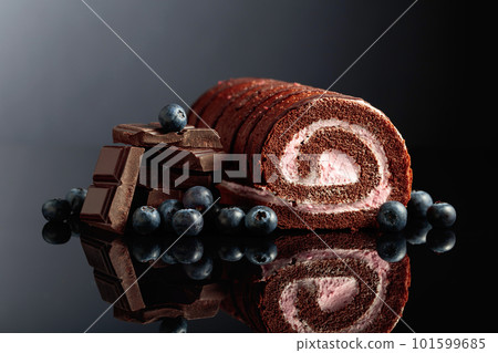 Chocolate roll cake with blueberries and a broken black chocolate bar. Chocolate roll cake with blueberries and a broken black chocolate bar. 101599685