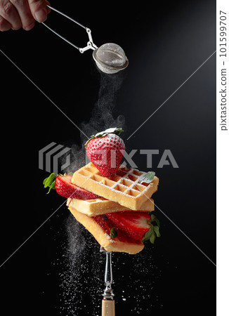 Waffles with strawberries sprinkled with sugar powder. 101599707