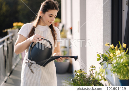 Woman watering the plants from a watering can. Young female watering the greens on balcony 101601419