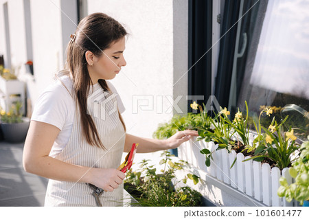 Smiled young female creating garden at balcony. Woman using a small spade to plant. Starting for landing 101601477