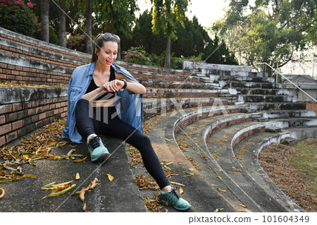Full length of sports woman checking fitness results or heart rate on smartwatch after running in the park Full length of sports woman checking fitness results or heart rate on smartwatch after running in the park 101604349