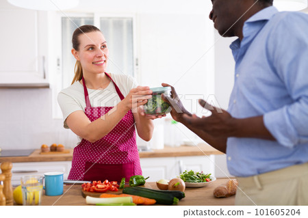 Smiling young wife giving container with salad to husband leaving for work 101605204