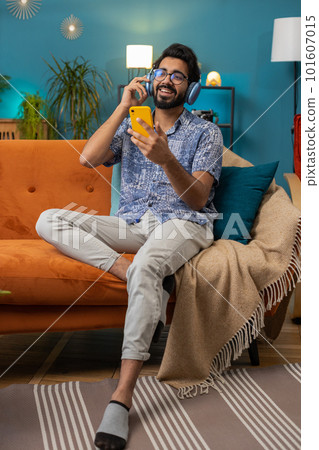 Happy indian man in wireless headphones relaxing sitting on sofa at home listening favorite music Happy indian man in wireless headphones relaxing sitting on sofa at home listening favorite music 101607015