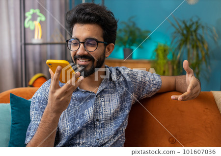Happy excited indian man making phone conversation talking with friend sitting call on couch at home 101607036