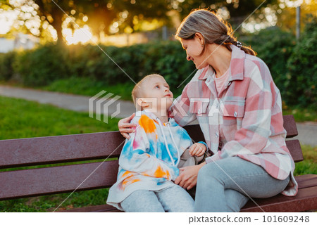 mother and son sit on a park bench in the rays of the setting sun. the concept of a family. Mother's Day. beautiful girl (mother) with a boy (son) in the park in the park are sitting on a bench at mother and son sit on a park bench in the rays of the setting sun. the concept of a family. Mother's Day. beautiful girl (mother) with a boy (son) in the park in the park are sitting on a bench at 101609248