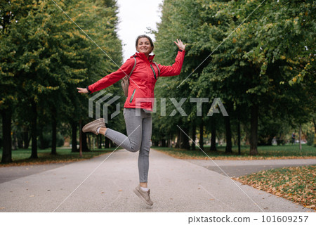 Young caucasian woman girl with toothy smile jumping in park forest outdoors looking at camera. Young caucasian woman girl with toothy smile jumping in park forest outdoors looking at camera. 101609257