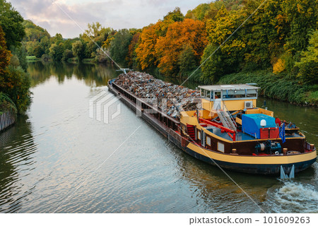 Transportation industry. Ship barge transports scrap metal and sand with gravel. Barge loaded with scrap metal is on the roadstead. Scrap metal transportation by water. Barge laden by metal salvage 101609263