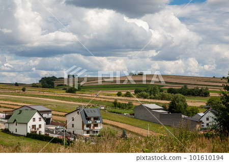 Countryside village. Rural scenery. Nature landscape. White cottage houses on meadow hills with yellow green field and fluffy sky clouds daylight panorama. 101610194