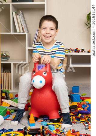 A little boy is jumping on an inflatable rubber donkey among the mess in the children's room. Bouncing toy for kids. 101612144
