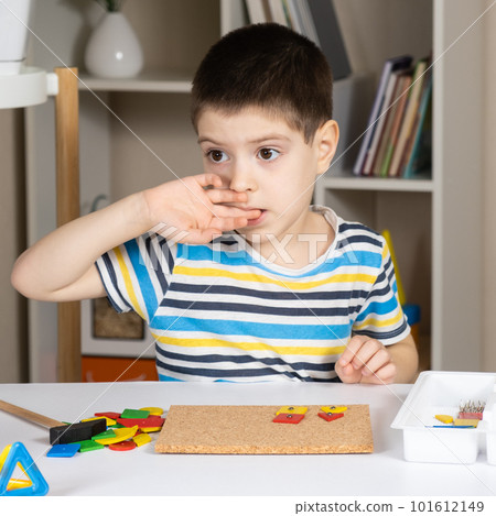 A 5-year-old boy bites his nails while sitting at a table and playing with mosaics in a children's room. Bad habits in children A 5-year-old boy bites his nails while sitting at a table and playing with mosaics in a children's room. Bad habits in children 101612149