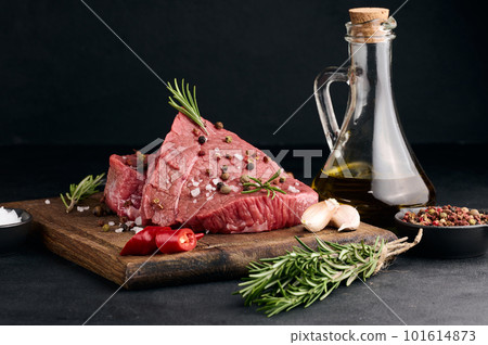 Raw piece of beef with spices pepper, rosemary sprig, salt and olive oil on a wooden board, black background Raw piece of beef with spices pepper, rosemary sprig, salt and olive oil on a wooden board, black background 101614873