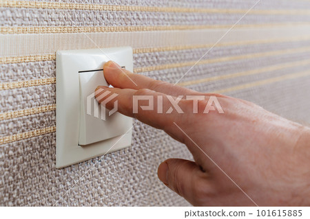 men's hand on White light switch on the wall with brown wallpaper. men's hand on White light switch on the wall with brown wallpaper. 101615885